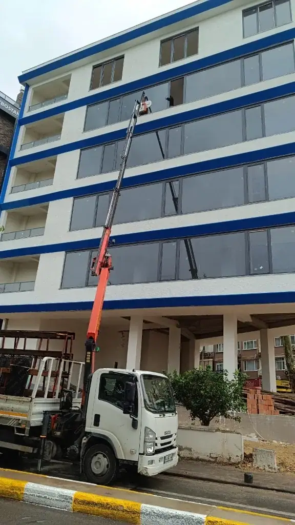 Çok katlı bir binanın cephesinde uzun bomlu vinçle cam montajı