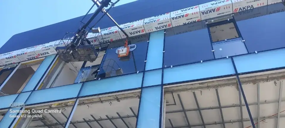 Dış cephede sepetli vinç ile mavi tonlu cam panellerin montajı