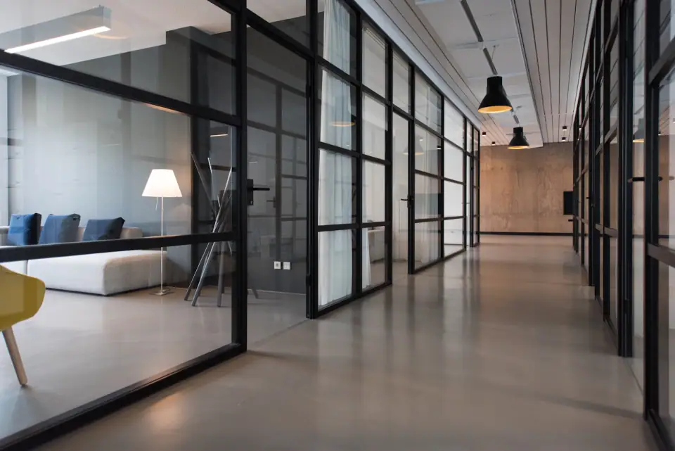 Siyah profilli cam bölmelerle ayrılmış aydınlık ofis koridoru
